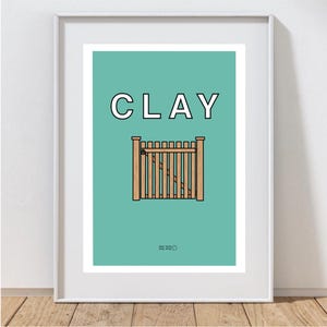 May include: A framed art print featuring the word "CLAY" in white block letters above a stylized illustration of a wooden gate. The background is a solid teal color. The print is in a white frame.