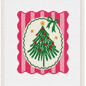 May include: A cross-stitch embroidery pattern on white fabric featuring a central oval with a green Christmas tree decorated with red ornaments and a yellow star. The oval is framed by a scalloped border and a pink and white striped background.