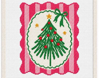 May include: A cross-stitch embroidery pattern on white fabric featuring a central oval with a green Christmas tree decorated with red ornaments and a yellow star. The oval is framed by a scalloped border and a pink and white striped background.