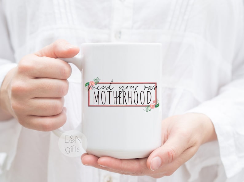 May include: White ceramic mug with a pink floral design and the text "Find your own motherhood" in a black rectangle with a pink border.