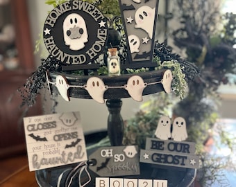 Könnte beinhalten: Ein schwarzes, mehrstöckiges Tablett, das mit Halloween-Dekorationen geschmückt ist. Das Tablett zeigt ein Schild mit der Aufschrift "Home Sweet Haunted Home", einen Sarg mit Geistern, eine Geistergirlande, ein Schild mit der Aufschrift "Wenn sich eine Tür schließt und eine andere öffnet, ist dein Haus wahrscheinlich verflucht", ein Schild mit der Aufschrift "Oh so spooky", ein Schild mit der Aufschrift "Be our ghost" und ein Schild mit der Aufschrift "Boo 2 U".