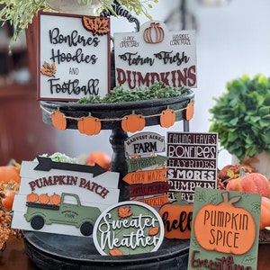 May include: A tiered tray decorated with fall-themed wooden signs. The signs feature phrases like "Bonfires Hoodies and Football", "Farm Fresh Dumpkins", "Pumpkin Patch", "Sweater Weather", and "Pumpkin Spice Everything".