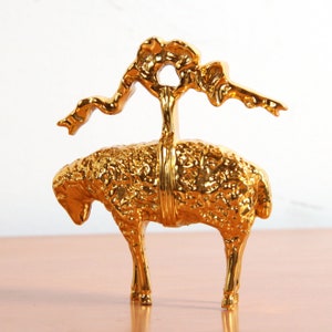 May include: A gold-colored metal sculpture of a sheep with a stylized tree growing from its back.