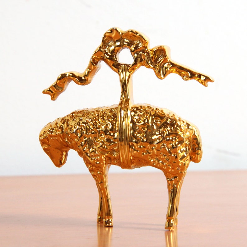 May include: A gold-colored metal sculpture of a sheep with a stylized tree growing from its back.
