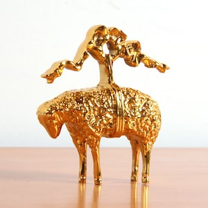 May include: A gold-colored metal sculpture of a sheep with a stylized tree growing from its back.