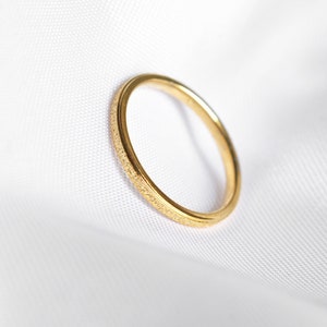 Könnte beinhalten: Ein goldener Ring mit strukturiertem Band, vor weißem Hintergrund. Die Oberfläche des Rings hat ein subtiles, gepunktetes Muster, und das Gesamtdesign ist schlicht und elegant. Der Ring ist ein Schmuckstück.