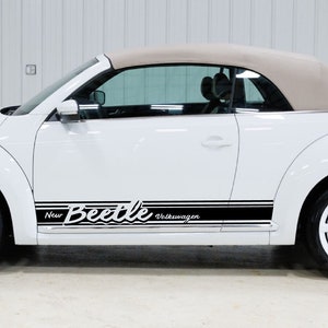 Puede incluir: Volkswagen New Beetle convertible blanco con rayas de carreras negras y las palabras "New Beetle Volkswagen" en el lateral.