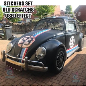Puede incluir: Volkswagen Beetle negro con una franja blanca y azul que recorre el capó y un número 53 blanco en el lateral. El coche tiene un portaequipajes y un efecto usado.