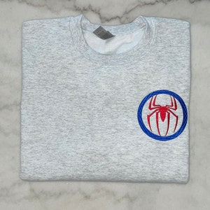May include: A heather gray sweatshirt with a red and blue embroidered Spiderman logo on the left side.