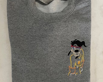 Op de afbeelding: Grijs sweatshirt met een cartoon hond met een zonnebril en een geel shirt geborduurd op de voorkant.