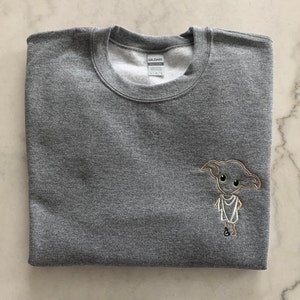 May include: A gray sweatshirt with an embroidered image of Dobby the house-elf from the Harry Potter series.
