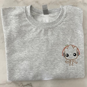 May include: A gray sweatshirt with a small embroidered image of a cartoon character wearing headphones. The character is brown and has a green leaf on its head. The character is standing in a pot.