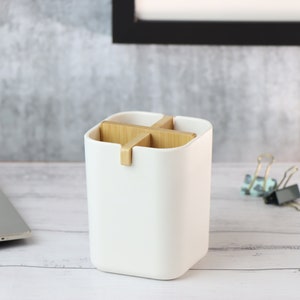 May include: White desk organizer with four compartments separated by wooden dividers. The organizer is on a white wooden surface.