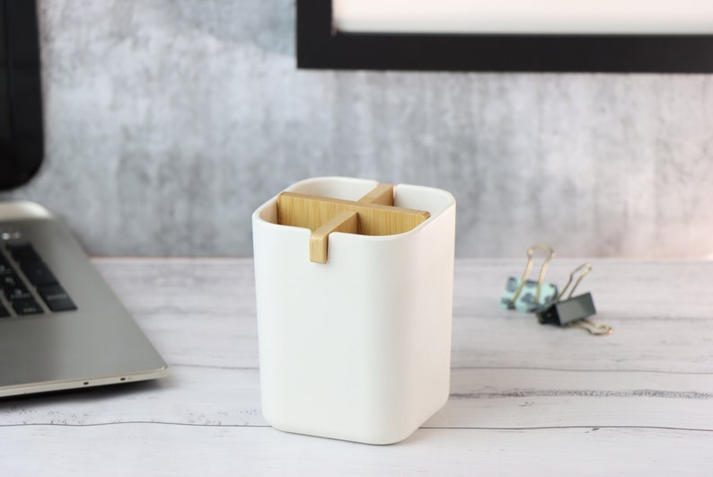 May include: White desk organizer with four compartments separated by wooden dividers. The organizer is on a white wooden surface.