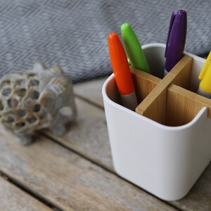 May include: White desk organizer with four compartments made of bamboo. The organizer holds five markers in orange, green, purple, and yellow.