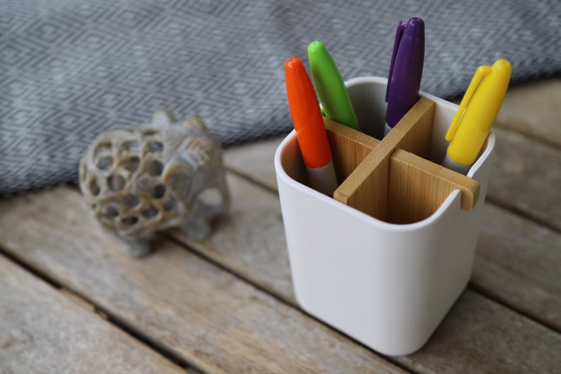May include: White desk organizer with four compartments made of bamboo. The organizer holds five markers in orange, green, purple, and yellow.