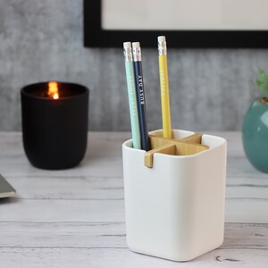 May include: White ceramic pencil holder with a wooden cross-shaped divider. Three pencils are in the holder, one blue, one green, and one yellow. Each pencil has a different word written on it: "Everyday", "Busy Day", and "Tuesday".