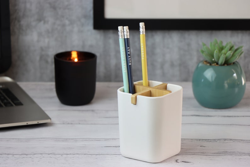 May include: White ceramic pencil holder with a wooden cross-shaped divider. Three pencils are in the holder, one blue, one green, and one yellow. Each pencil has a different word written on it: "Everyday", "Busy Day", and "Tuesday".