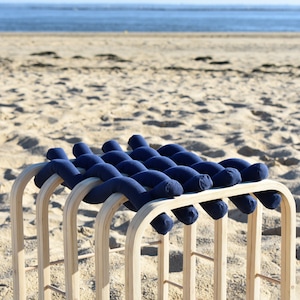 May include: A wooden frame with a woven blue fabric seat. The seat is made of multiple blue fabric tubes that are woven together to create a comfortable and unique design. The frame is made of natural wood and has a simple, elegant design.