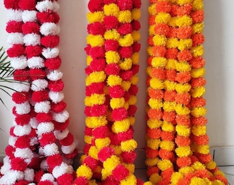 Könnte beinhalten: Drei Stränge bunter Ringelblumen-Girlanden. Ein Strang ist rot und weiß, der zweite ist rot und gelb und der dritte ist orange und gelb. Die Girlanden bestehen aus kleinen, runden, flauschigen Blüten und hängen vertikal.