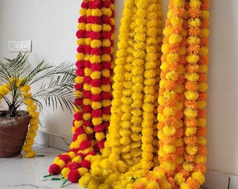 Könnte beinhalten: Drei Girlanden aus Ringelblumen in leuchtenden Farben. Eine Girlande wechselt sich mit Rot und Gelb ab, eine andere ist einfarbig gelb, und die dritte geht von Gelb zu Orange über. Die Girlanden hängen an einer weißen Wand.