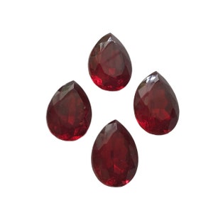 Puede incluir: Cuatro gemas facetadas, en forma de lágrima, de color rojo intenso, dispuestas sobre un fondo blanco. Las gemas tienen un corte brillante, que refleja la luz. Estas gemas podrían usarse para hacer joyas u otros proyectos de artesanía.