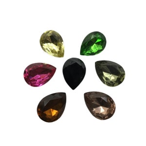 May include: Seven teardrop-shaped glass beads in various colors, including green, pink, yellow, brown, black, and clear. The beads are arranged in a circle on a white background.