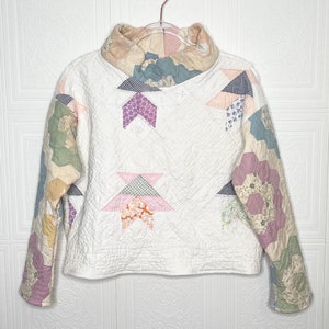 以下が含まれることがあります： ハイネックと長袖の白いキルティングジャケット。ジャケットは、ピンク、パープル、ブルー、グリーンなど、さまざまな色とパターンでパッチワーク生地で作られています。