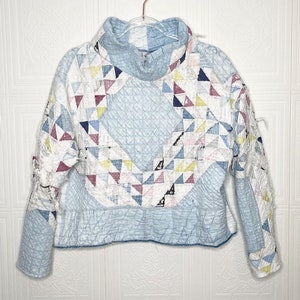 May include: A blue and white patchwork quilt jacket with a high neck and long sleeves.