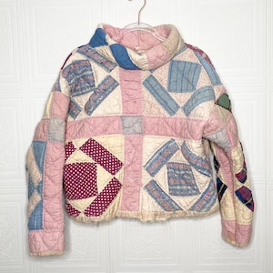 May include: A pink, blue and white quilted jacket with a patchwork design. The jacket has a high neck and a cropped length.