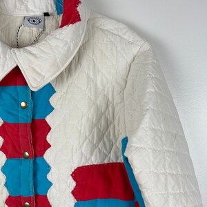 Puede incluir: Una chaqueta acolchada blanca con un dise&ntilde;o de patchwork con cuadrados rojos y azules. La chaqueta tiene un cierre de botones y un cuello.