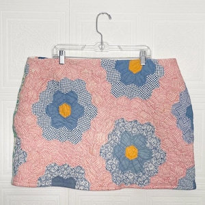 以下が含まれることがあります： ピンクとブルーのパッチワークスカートで、花柄のデザインです。スカートはキルティング生地で作られており、フリルのあるヘムラインです。