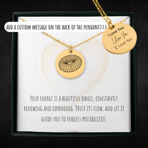 May include: A gold necklace with a pendant featuring a geometric design. The pendant is in a box with a message that reads "Your energy is a beautiful dance, constantly renewing and expanding. Trust its flow, and let it guide you to endless possibilities."
