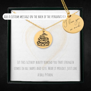 May include: Gold-colored pendant necklace featuring a detailed engraving of a ball python on a circular charm. A second charm reads "I love you so much". The necklace is presented in a gift box with text.