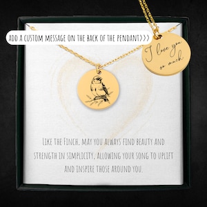 May include: A gold necklace with two round pendants. One pendant features a black and white illustration of a bird on a branch. The other pendant has the handwritten message "I love you so much".