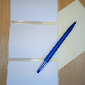 May include: Three white adhesive labels on a sheet with a blue pen on top of the sheet.