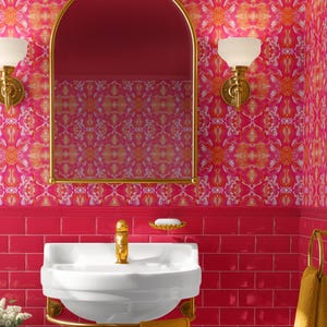 Könnte beinhalten: Ein lebendiges, pinkfarbenes Badezimmer mit gemusterter Tapete und passenden Fliesen. Ein weißes Standwaschbecken mit goldenen Armaturen und einem gelben Handtuch. Ein goldgerahmter Spiegel und Wandleuchten. Ein kleiner rosa Hocker trägt eine gelbe Vase.