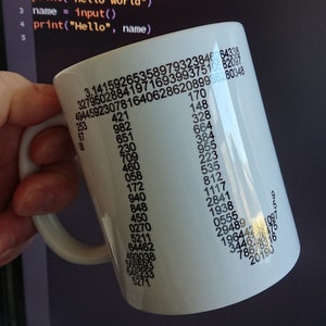 Puede incluir: Taza de cerámica blanca con asa, cubierta de números negros y el comienzo del número Pi. La taza se sostiene frente a una pantalla de ordenador que muestra código. El código incluye el texto "hello world".