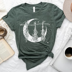 Pu&ograve; includere: T-shirt verde scuro con un design a mezzaluna bianca adornato con erbe sospese e stelle. La maglietta &egrave; realizzata in un tessuto morbido e ha un girocollo. Il design ha un tema vintage e celeste.