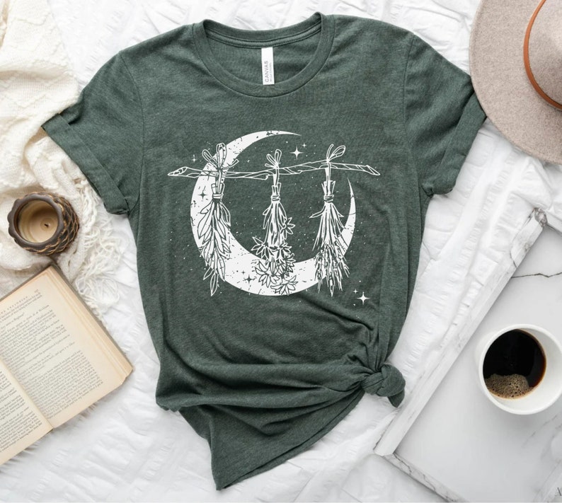 Pu&ograve; includere: T-shirt verde scuro con un design a mezzaluna bianca adornato con erbe sospese e stelle. La maglietta &egrave; realizzata in un tessuto morbido e ha un girocollo. Il design ha un tema vintage e celeste.