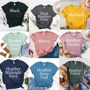 May include: Nine different color t-shirts with text describing the color of each shirt. The colors are black, dark heather gray, mustard, heather prism dust, mauve, heather orchid, heather midnight navy, heather deep teal, and heather forest.