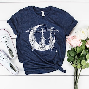 Pu&ograve; includere: T-shirt blu navy con un design a mezzaluna bianca ed elementi botanici sospesi. Sono presenti anche scarpe da ginnastica bianche e un bouquet di rose rosa e bianche. La maglietta &egrave; annodata in vita.