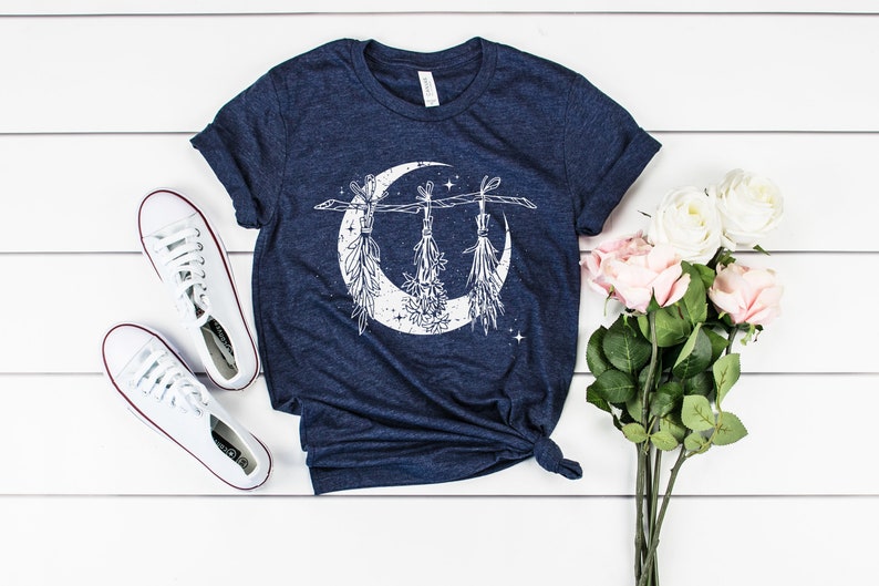 Pu&ograve; includere: T-shirt blu navy con un design a mezzaluna bianca ed elementi botanici sospesi. Sono presenti anche scarpe da ginnastica bianche e un bouquet di rose rosa e bianche. La maglietta &egrave; annodata in vita.