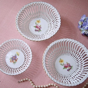 Könnte beinhalten: Drei weiße Porzellanschalen mit geflochtenem Design und floralen Akzenten. Die Schalen sind ineinander verschachtelt, wobei die größte Schale oben und die kleinste unten liegt.