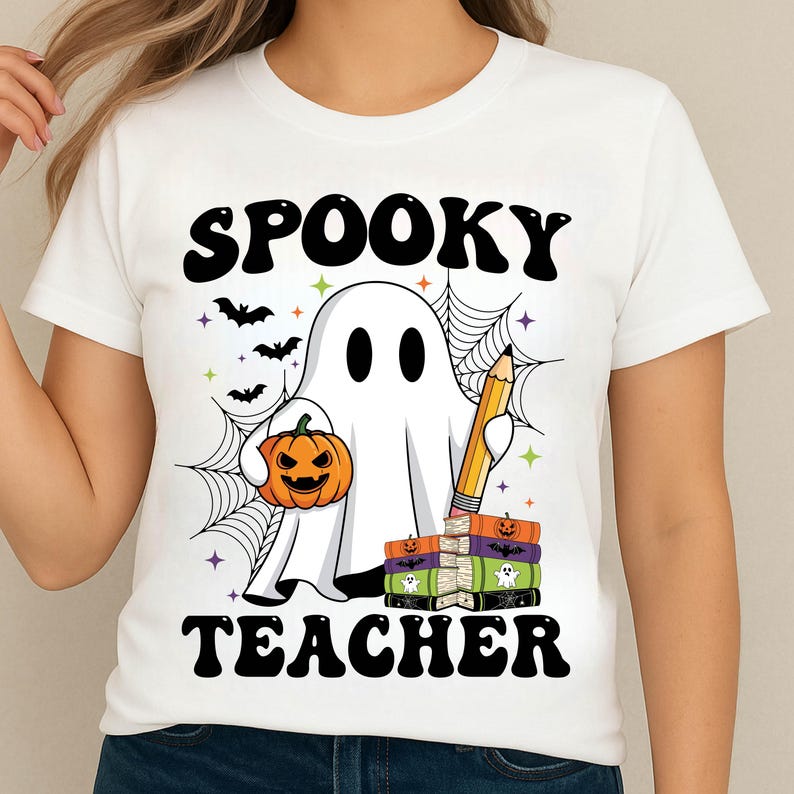 May include: White t-shirt with a Halloween-themed graphic. The design features a cartoon ghost holding a pumpkin and a pencil, with the words "Spooky Teacher" in black. Bats, spiderwebs, and stars complete the design.
