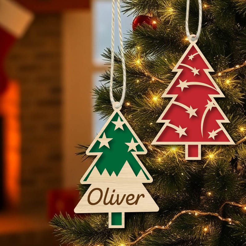 K&ouml;nnte beinhalten: Zwei h&ouml;lzerne Weihnachtsbaumschmuckst&uuml;cke, die an einem Weihnachtsbaum h&auml;ngen. Das Ornament links ist gr&uuml;n mit wei&szlig;en Sternen und dem Namen "Oliver" darauf geschrieben. Das Ornament rechts ist rot mit wei&szlig;en Sternen und wei&szlig;en Linien.