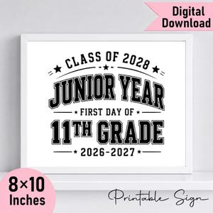 May include: A white rectangular sign with black text that reads CLASS OF 2028, JUNIOR YEAR, FIRST DAY OF 11TH GRADE, and 2026-2027. The design features stars and bold lettering in a collegiate style, presented within a simple white frame.