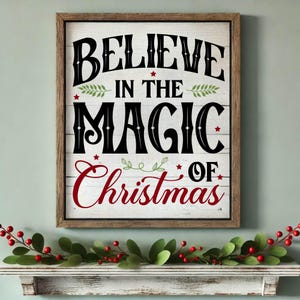 Könnte beinhalten: Ein Holzschild mit dem Text "Believe in the Magic of Christmas" in schwarzer und roter Schrift mit grünen Blättern und roten Sternen.