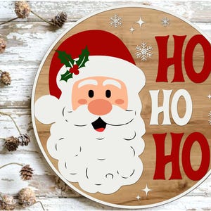 May include: Round wooden Christmas sign featuring Santa Claus with a red hat and the words "HO HO HO" in red. The sign has a light wood grain background with white snowflakes and stars.