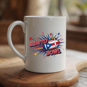 May include: White ceramic mug featuring the words "BENITO BOWL" in a comic book style font. The design includes a football with the Puerto Rican flag and starbursts in red, blue, and yellow. The mug has a curved handle.